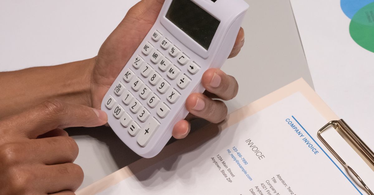 Close-up of hands using a calculator next to a company invoice, depicting a financial calculation concept. — illustrating expenses reciept