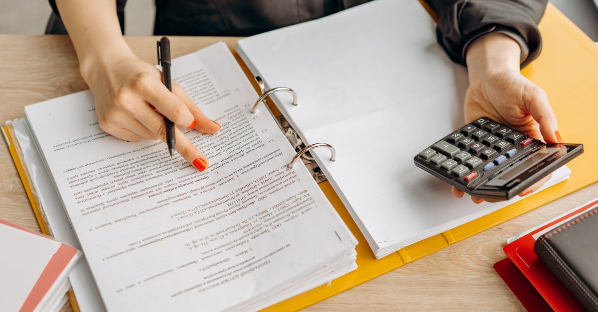 A woman reviewing documents and using a calculator on a wooden table. — illustrating expensesrecipt