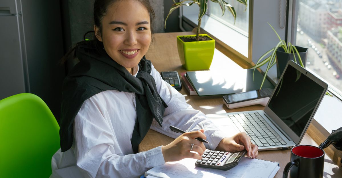Confident woman working with calculator in bright office setting, surrounded by office tools. — illustrating expensesrecipt
