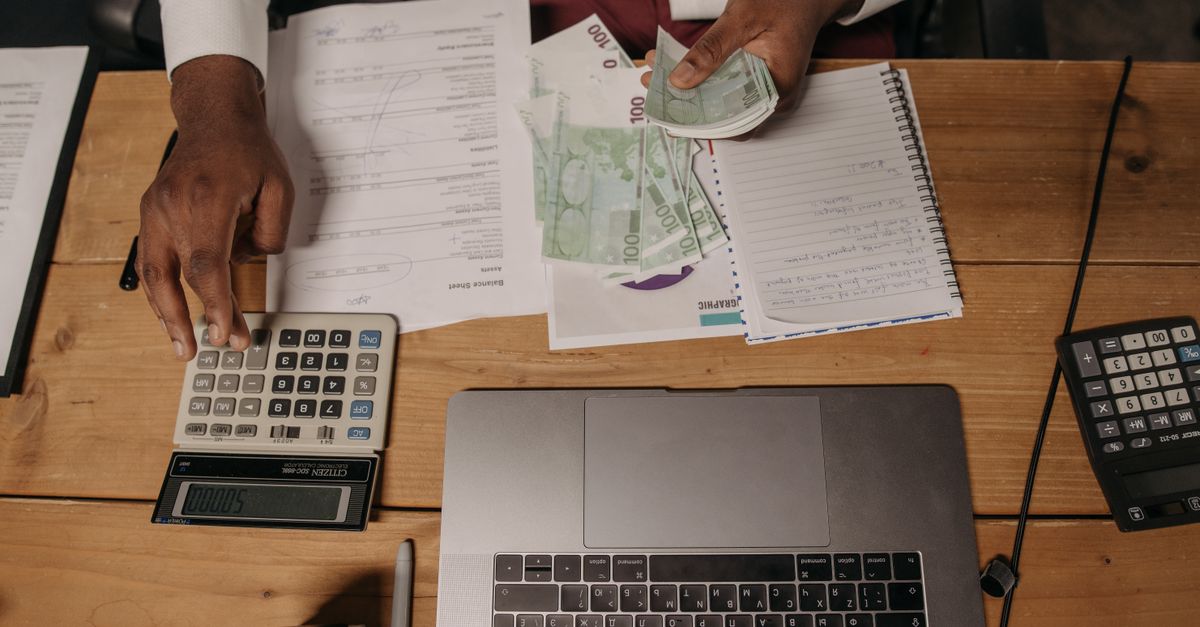 Close-up of a person counting cash with documents and a laptop in an office setting. — illustrating express expenses