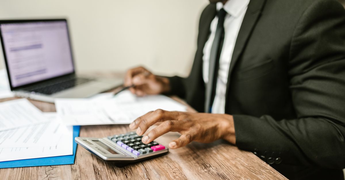 A businessman in a black suit using a calculator at a desk with financial documents and a laptop. — illustrating express expenses