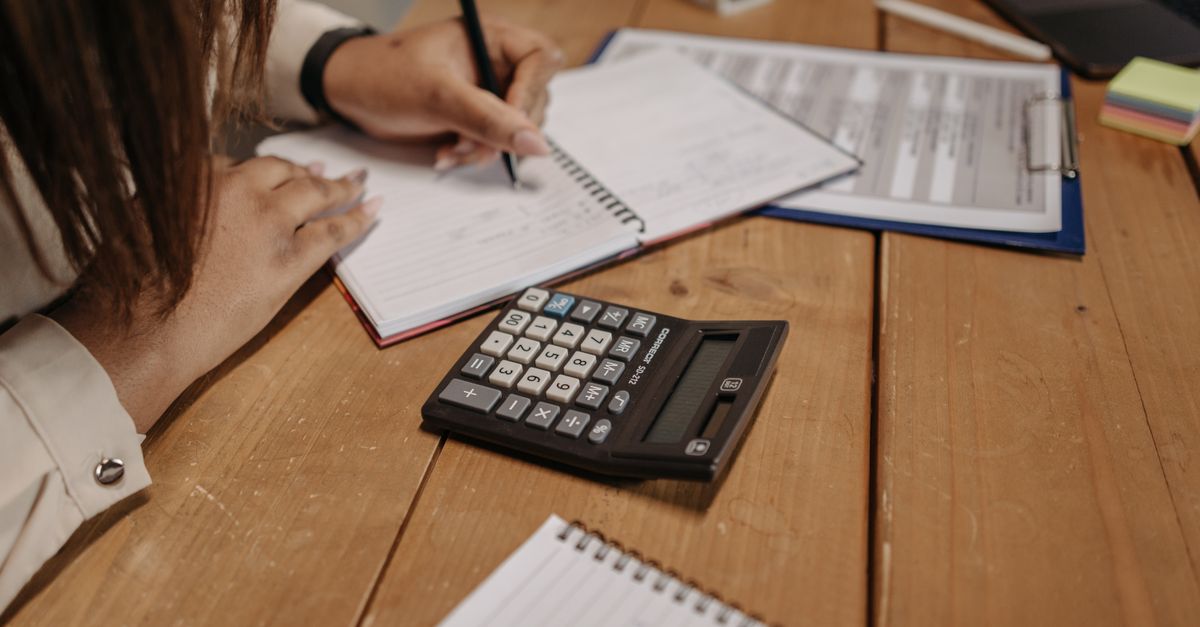 Woman writing notes with a calculator on a wooden desk, focusing on work and accounting. — illustrating fake recipt maker
