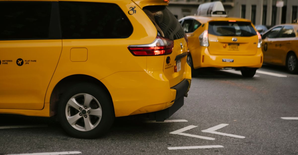 Modern yellow crossover taxi cars riding on asphalt road near commercial buildings in city — illustrating free fake cab