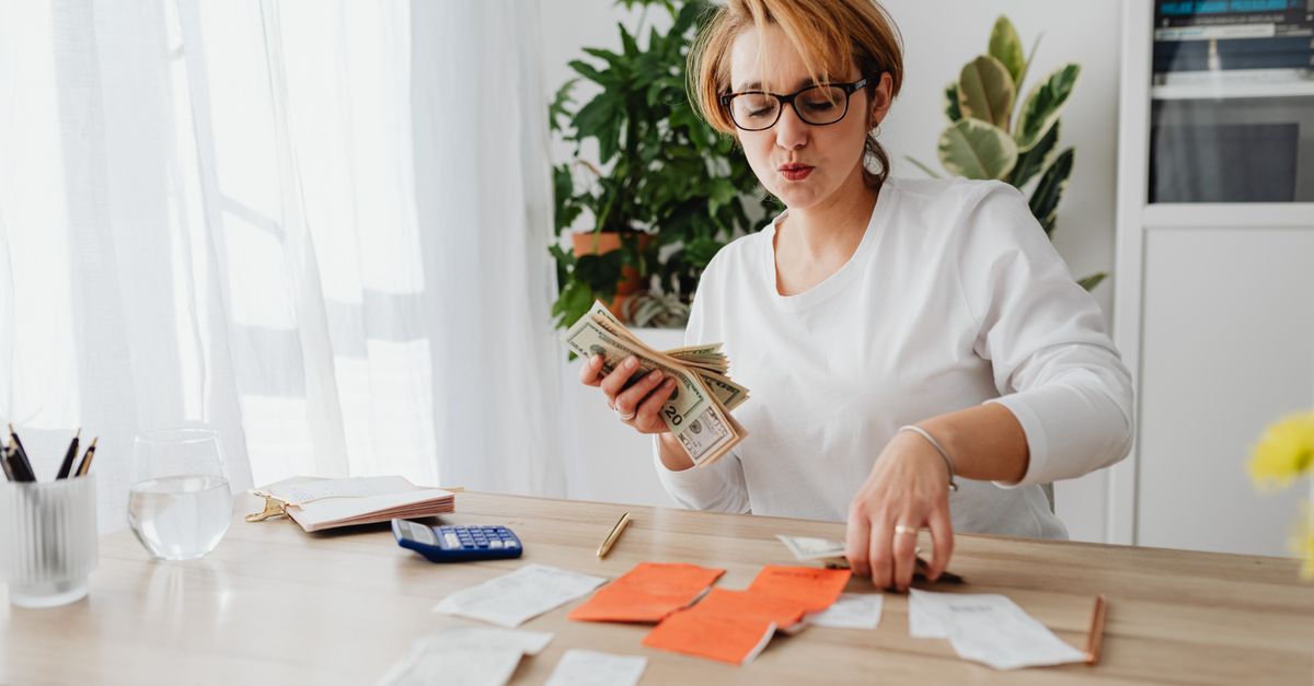 Woman sitting at a table counting cash and organizing receipts with a calculator nearby. — illustrating gas receipt