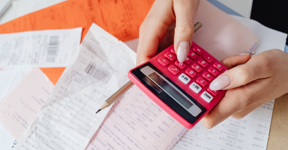 Hands using a pink calculator to manage expenses amidst various receipts and documents. — illustrating gas receipt