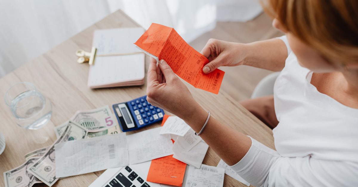Woman using calculator and receipts at home office desk for finance management. — illustrating how can i make a fake receipt