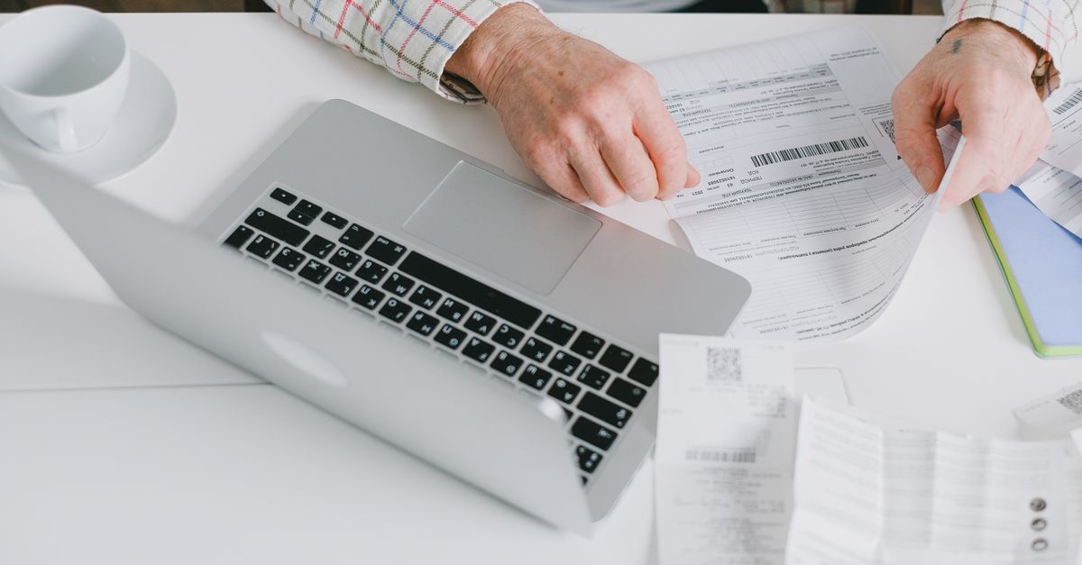 Close-up of hands organizing documents on a desk with a laptop. — illustrating how can i make a fake receipt