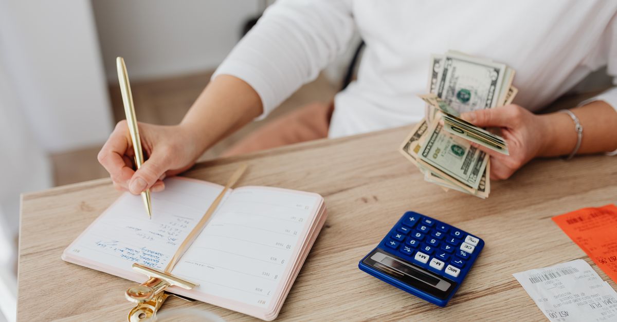 Adult holding cash and writing in planner while using a calculator at home. — illustrating expensive receipts