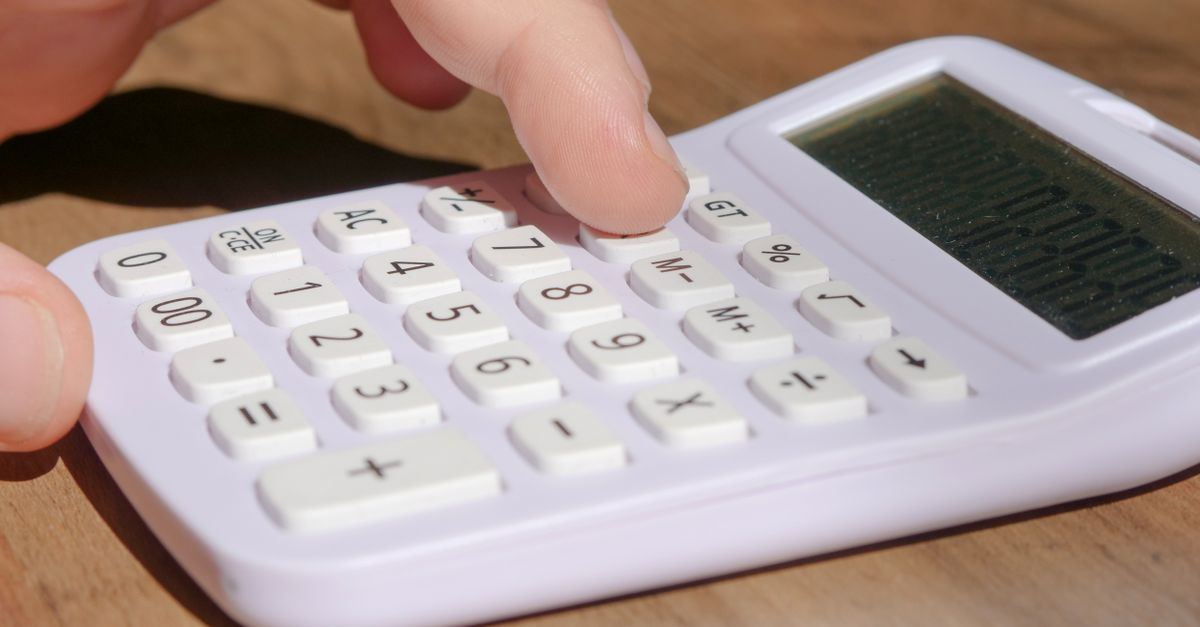 A hand pressing keys on a white calculator placed on a wooden desk in bright daylight. — illustrating expenses receipt