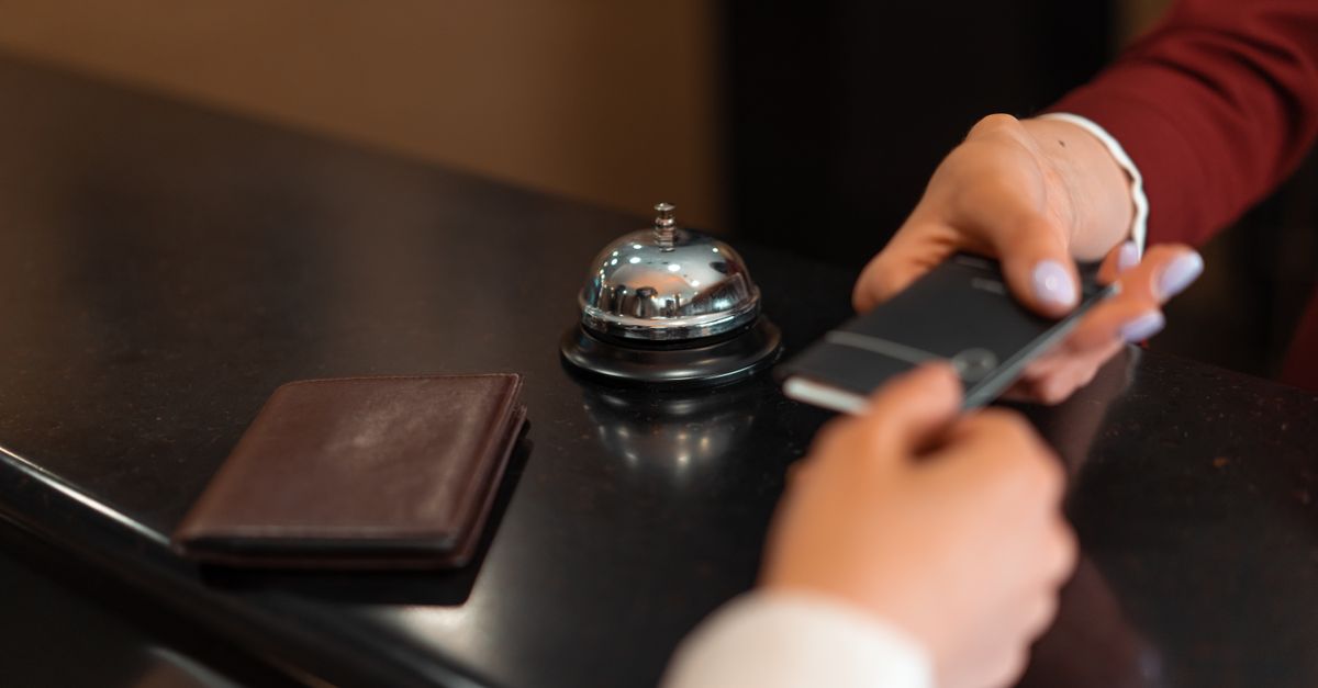 A close-up of a hotel check-in process with a smartphone and card transaction at the reception desk. — illustrating airbnb receipt generator