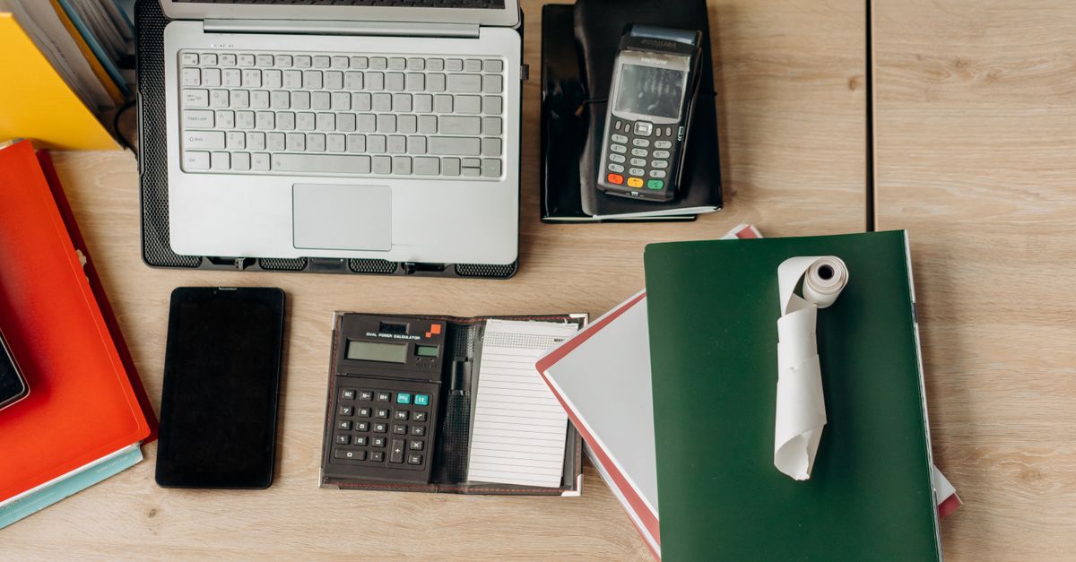 An organized office desk featuring a laptop, calculator, payment terminal, and documents. — illustrating online receipt generator