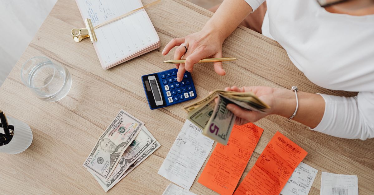 Overhead view of a person using a calculator to manage cash and receipts at a desk. — illustrating receipt making